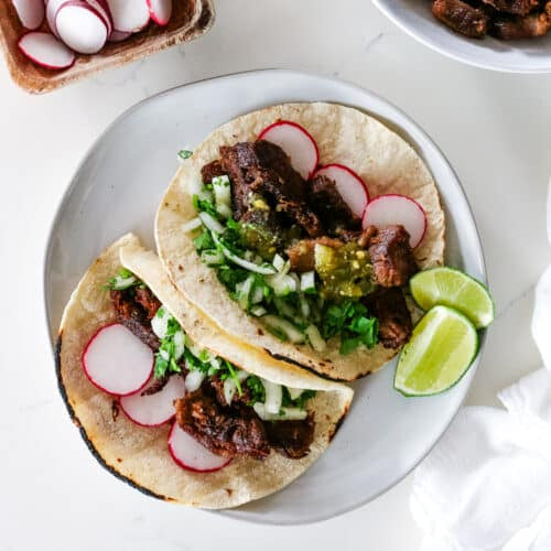Tacos de Lengua (beef tongue tacos) garnished with cilantro and lime wedges (radish slices optional).