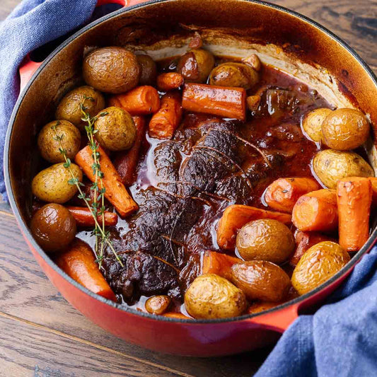 Classic pot roast with beef, carrots, and potatoes cooking in a Dutch oven